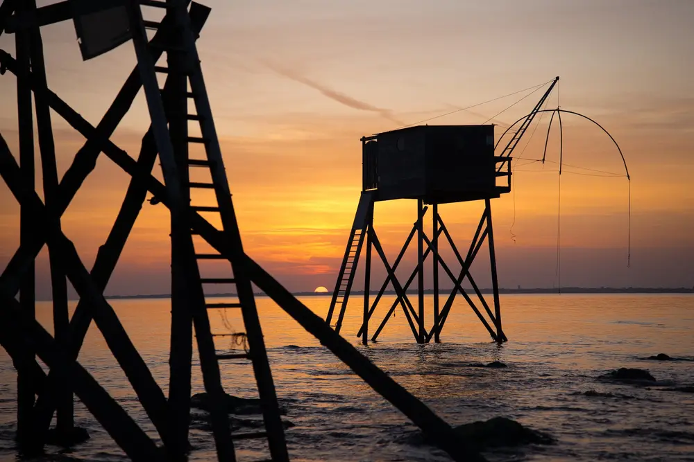 Carrelet de pêche et son filet découpés sur un ciel orangé au crépuscule