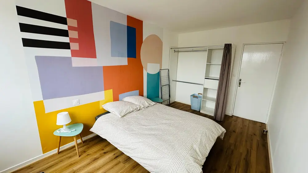 Chambre lumineuse décorée d'une grande fresque géométrique aux couleurs vives