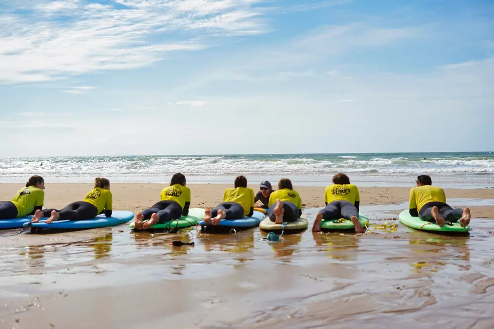 Groupe de surfeurs débutants allongés sur leurs planches au bord de l'océan