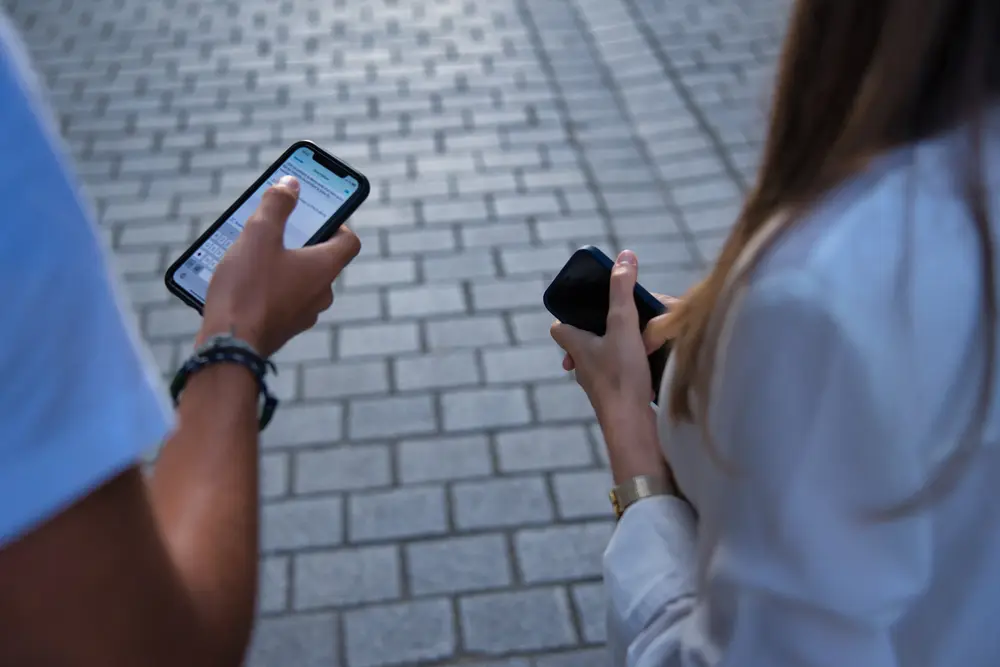 Gros plan sur deux professionnels consultant leur téléphone sur un parvis pavé