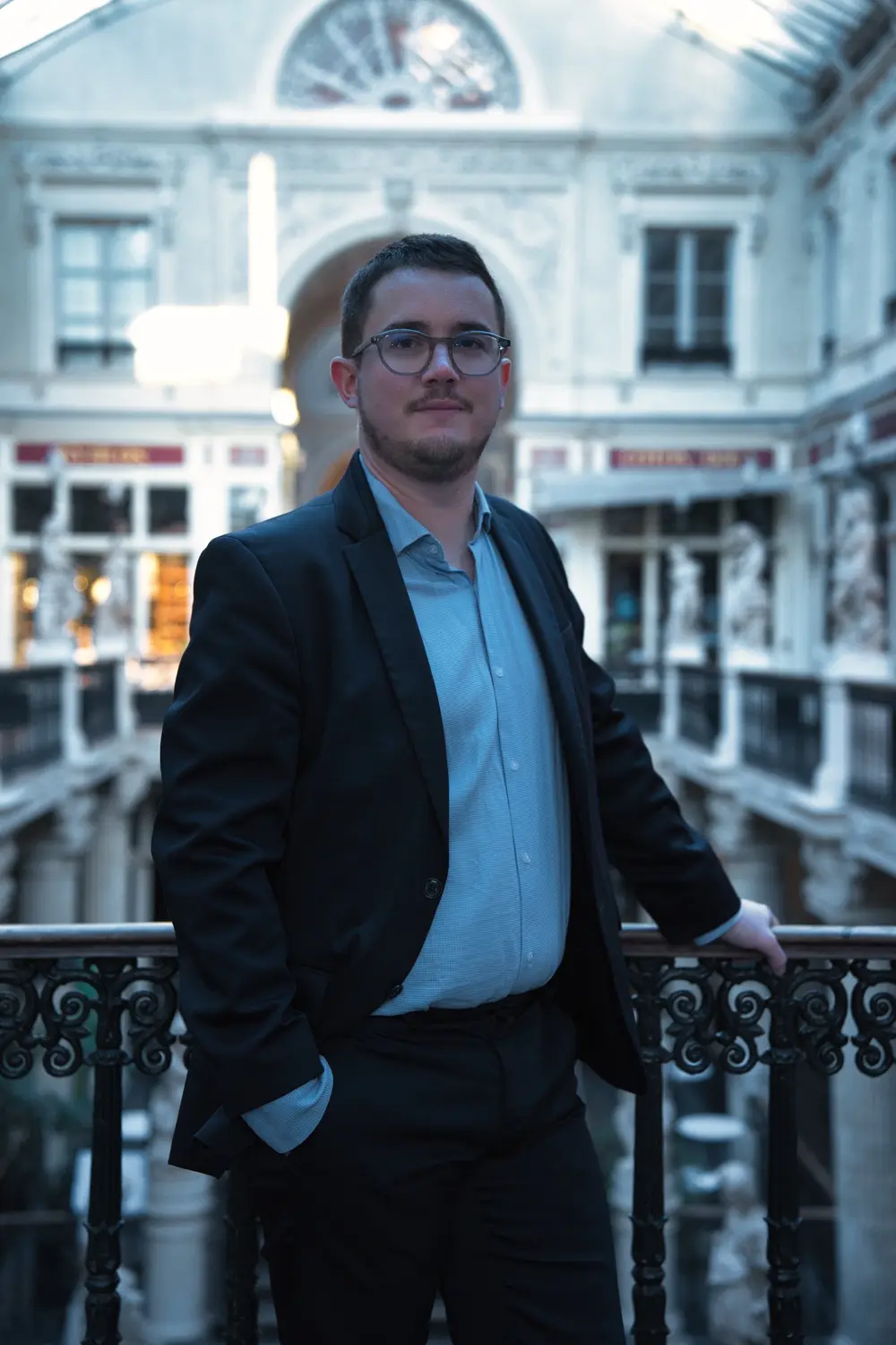 Portrait d'un notaire en veste sombre, la main sur la rambarde en fer forgé du passage Pommeraye