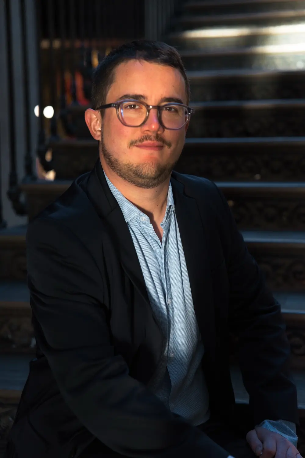Portrait d'un notaire à lunettes assis sur le grand escalier, éclairé par la lumière naturelle