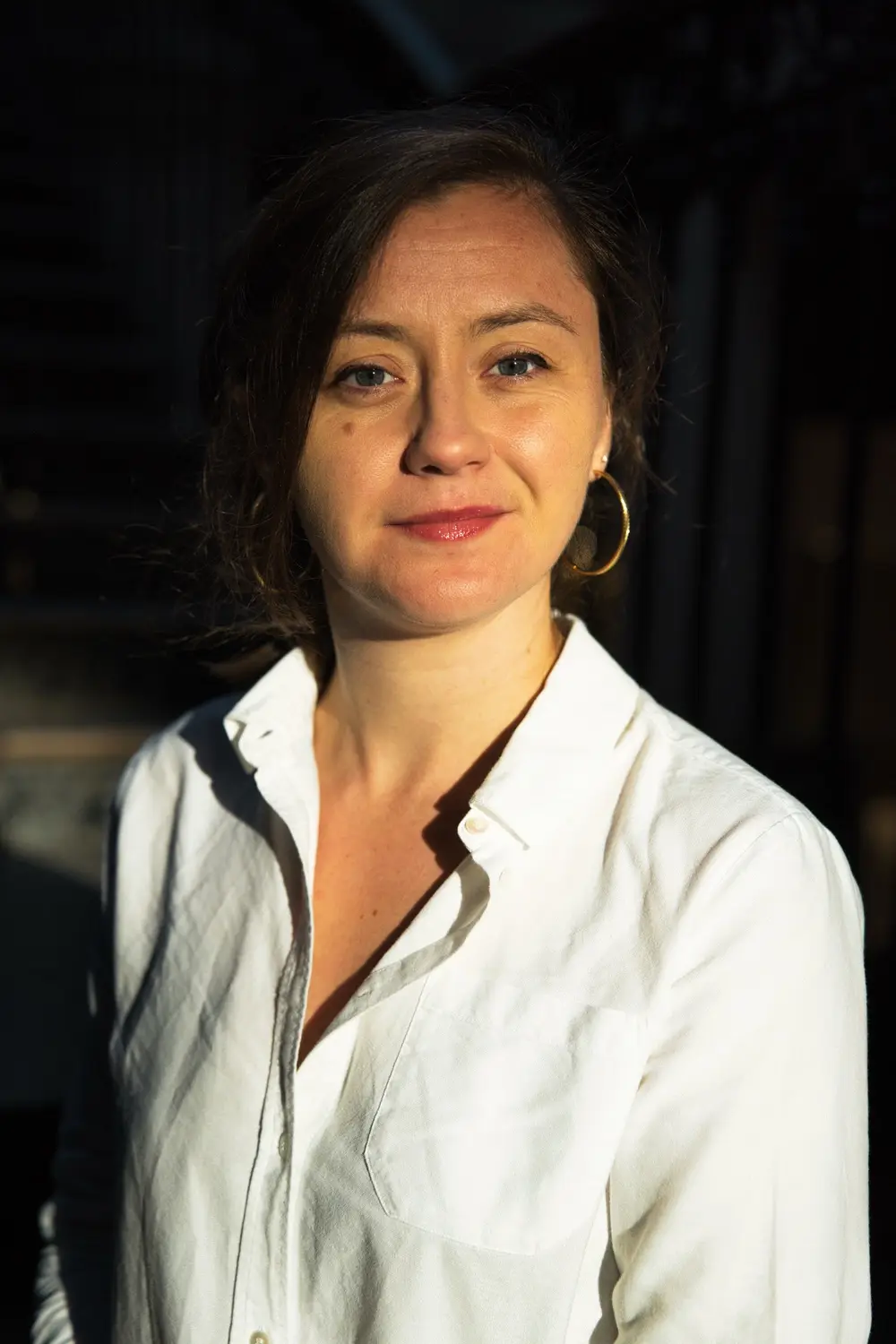 Portrait serré d'une notaire souriante en chemise blanche, dans un rayon de soleil