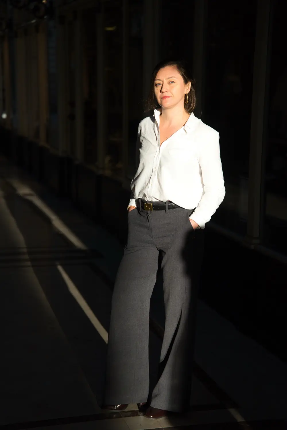 Portrait en pied d'une notaire en pantalon large, dans un rai de lumière du passage Pommeraye
