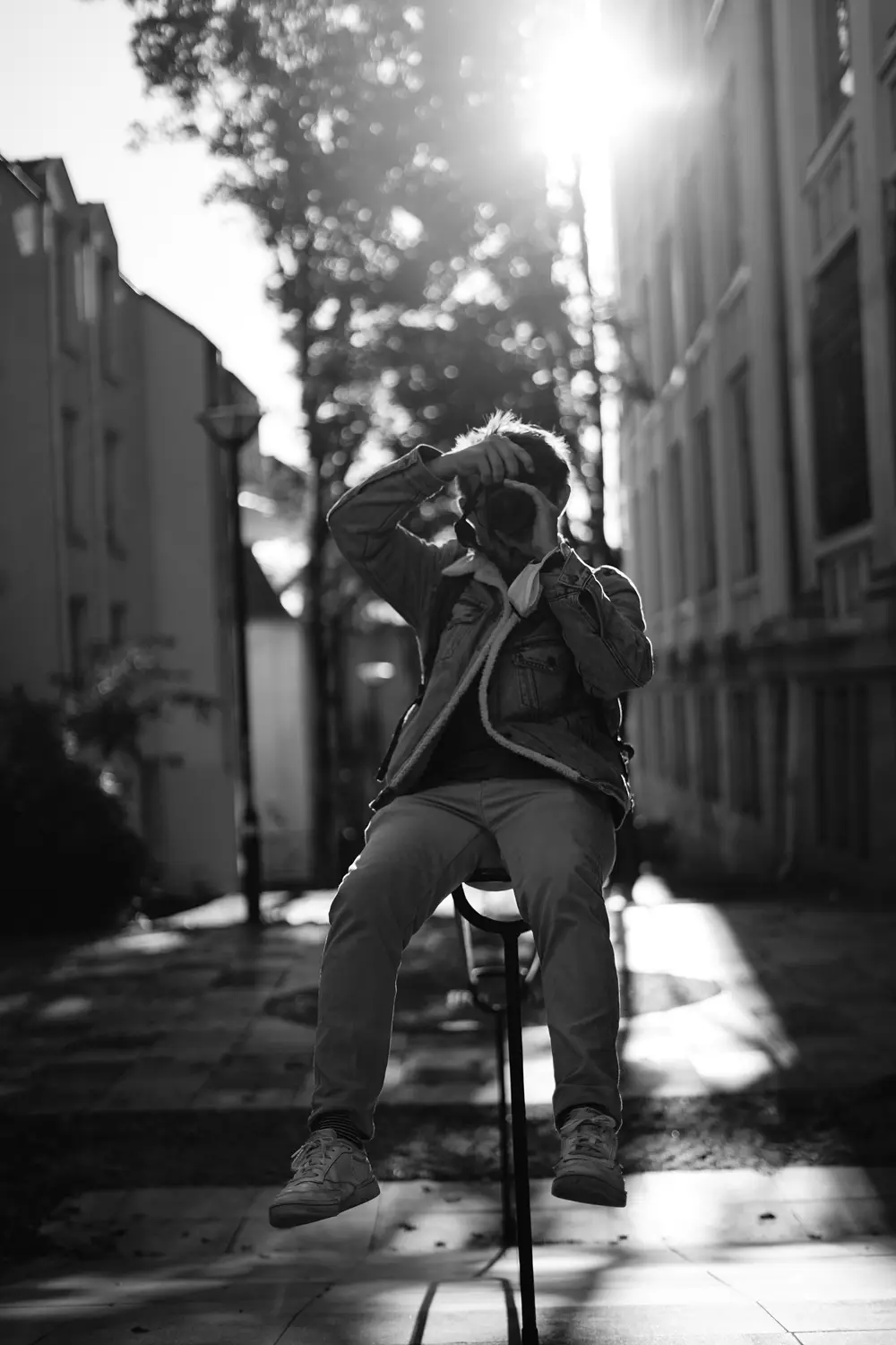 Jeune homme assis sur un poteau, appareil photo en main, dans une ruelle