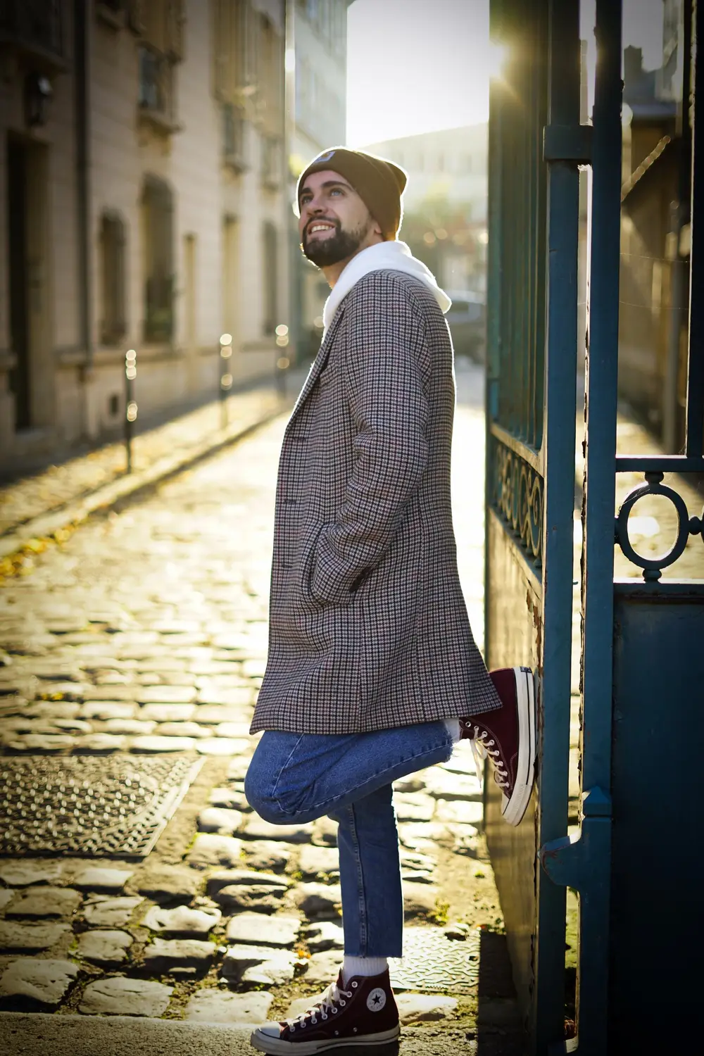 Portrait d'un homme en manteau adossé à un portail dans une ruelle pavée
