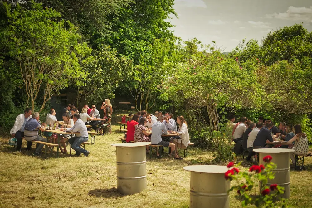 Repas d'équipe en plein air sur de grandes tables en bois dans un jardin