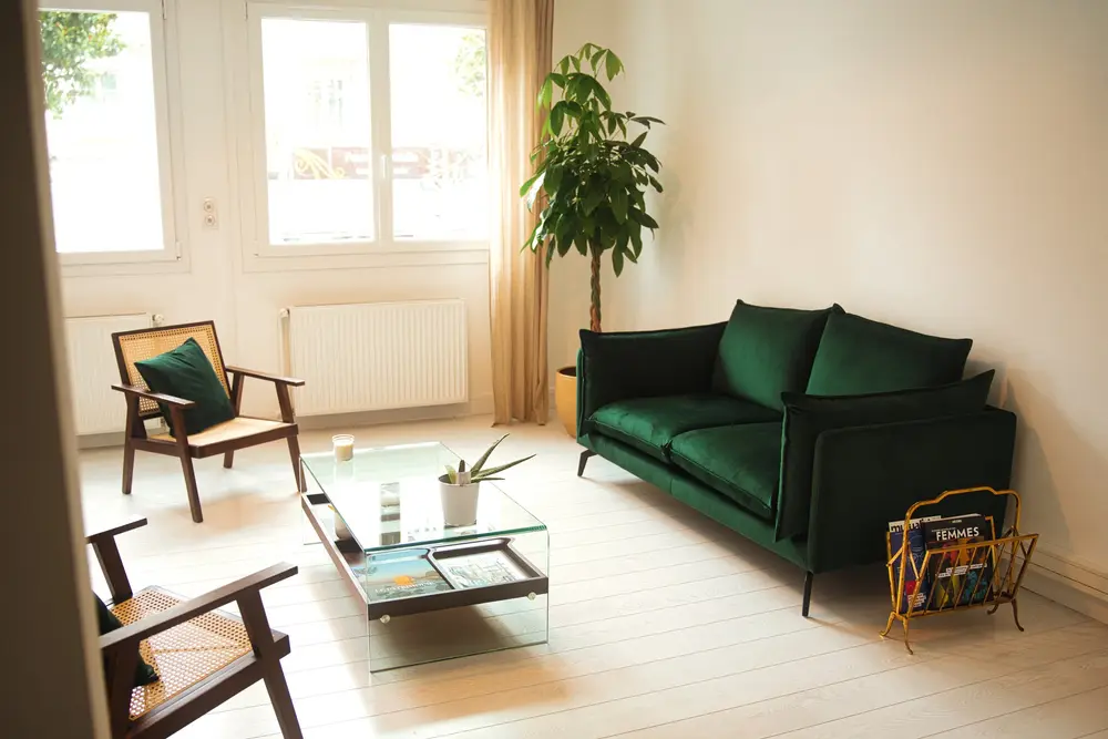 Canapé en velours vert et table basse en verre dans un salon clair